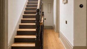 Una scala con gradini in legno e una ringhiera scura, che conduce a un pianerottolo con soffitto bianco e lampadari.