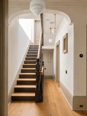 A staircase with wooden steps and a dark balustrade, leading to a landing with a white ceiling and pendant lights.