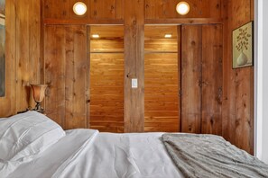 A wooden-paneled room with a bed, a nightstand, a lamp, and a framed picture on the wall. - NEW! City Explorer Basecamp Buffalo (Buffalo)