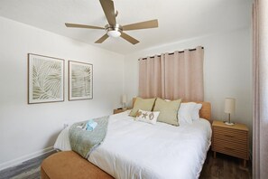 Ein Schlafzimmer mit einem Bett, zwei Nachttischen, einem Deckenventilator und zwei Wandbildern.