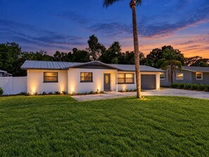 Ein eingeschossiges Haus mit Garage, Rasen und einer Palme.