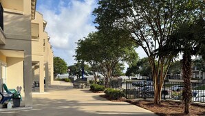 A paved walkway with a bench, a flag, and a palm tree. - No Egrets: 2 BR Condo Gulf Views, Pool, Walk to Beach, Golf Cart District (Long Beach)