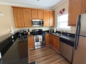 A kitchen with wooden cabinets, stainless steel appliances, a black countertop, and a window with blinds.