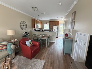 Ein Wohnzimmer mit rotem Sofa, ein Essbereich mit Tisch und Stühlen, eine Küche mit Holzschränken und einem Kühlschrank sowie eine Tür, die nach draußen führt.