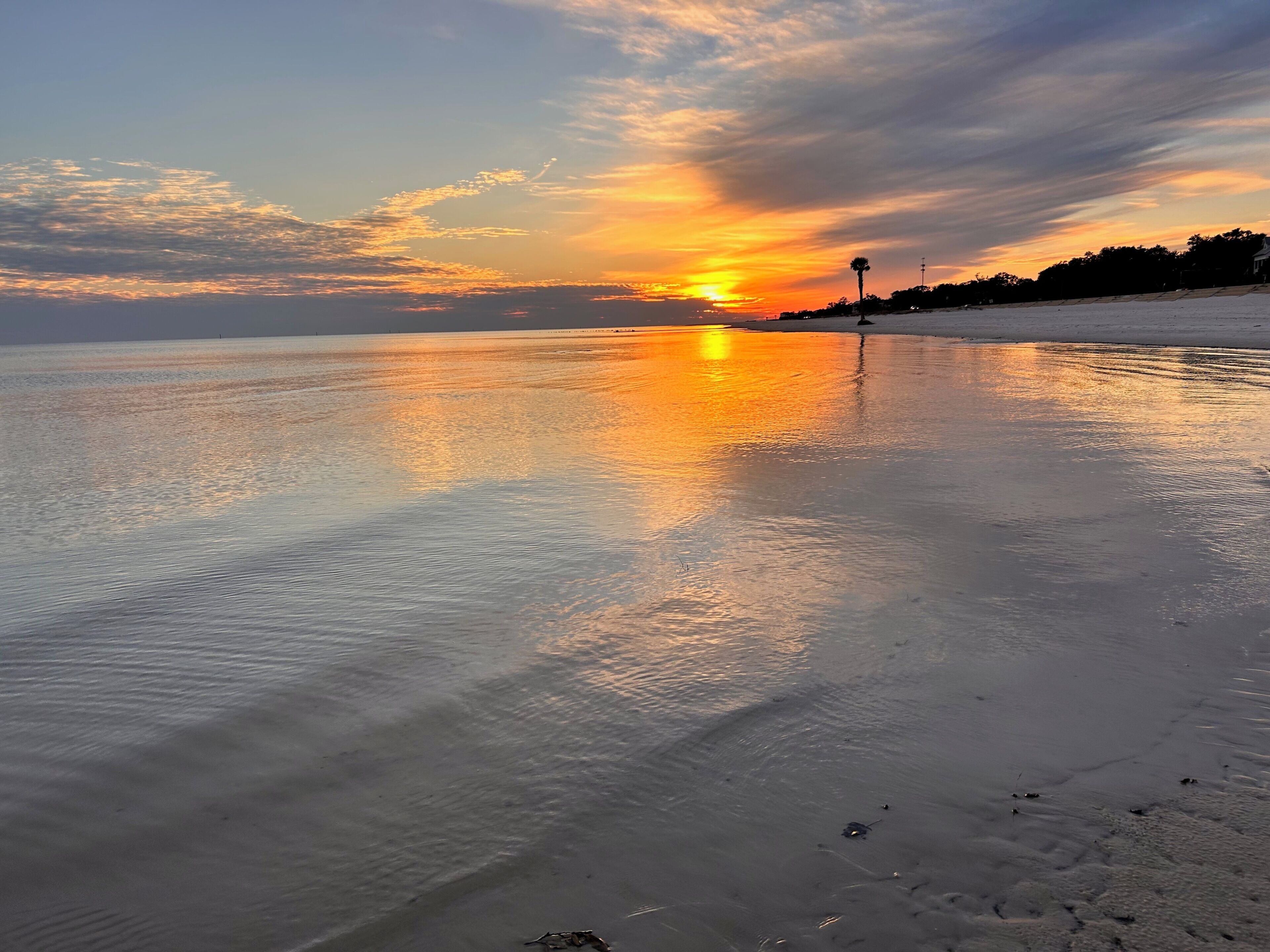 Ein Strand mit ruhigem Wasser, das den Sonnenuntergang widerspiegelt.