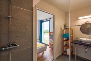 Ein modernes Badezimmer mit Duschkabine aus Glas, einem Nachttisch aus Holz, einer kleinen Ablage für Toilettenartikel und einem großen Spiegel.