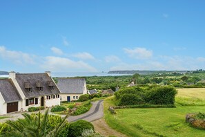 Paisaje rural con una casa blanca, un camino sinuoso y vista al mar.