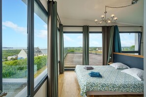 Quarto com uma grande janela, uma cama e vista para o campo.