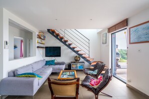 Una sala de estar moderna con un sofá, una mesa de centro y sillones de cuero, una escalera y un ventanal grande.