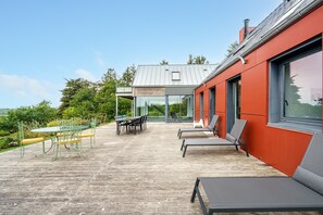 Un patio moderno al aire libre con una mesa y sillas de comedor, una zona de estar con sillones reclinables y una estructura de cristal.