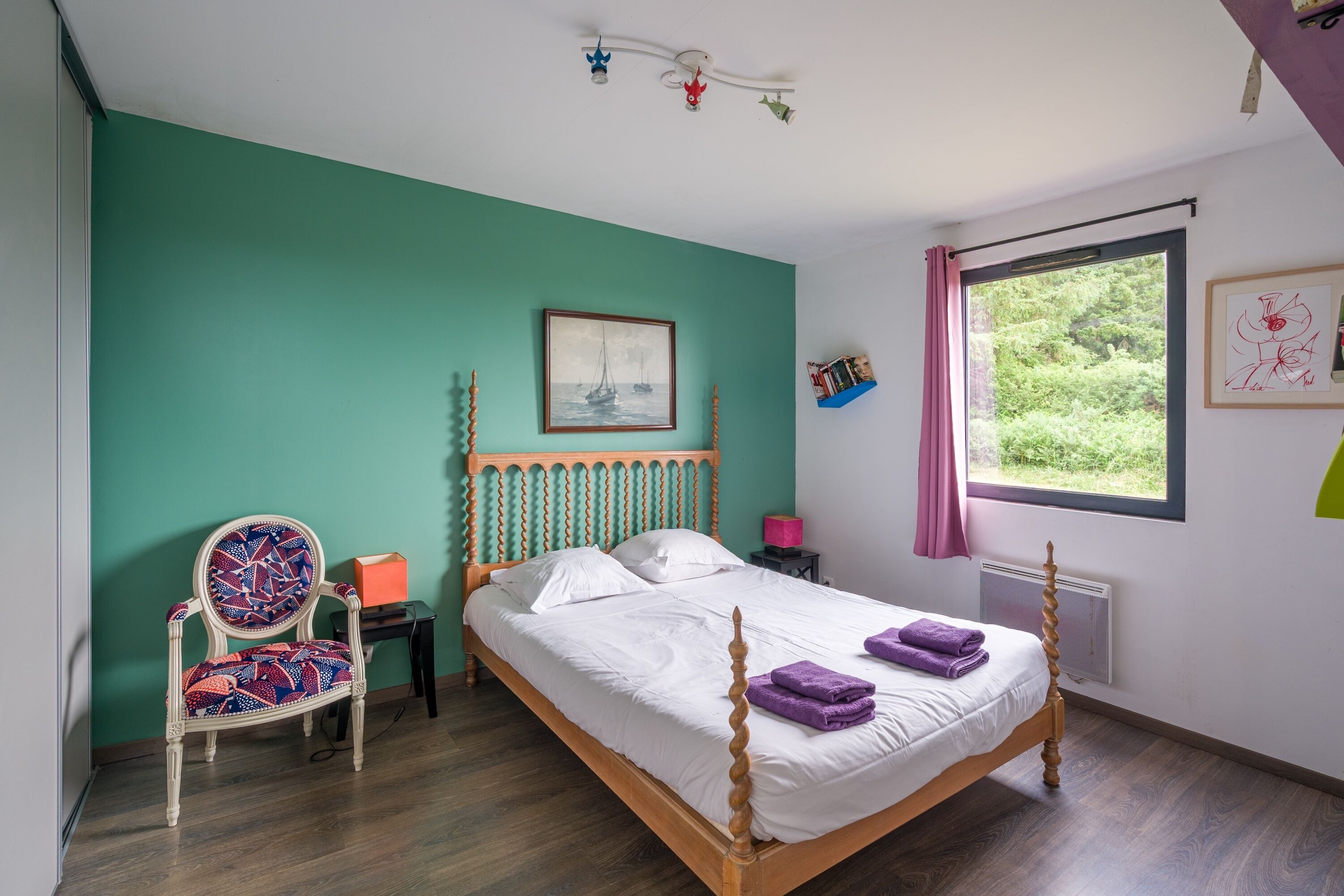 A bedroom with a bed, a chair, a window, and a painting on the wall.