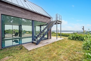 Et moderne hus med en glasfacade, en træterrasse og en trappe op til en balkon.