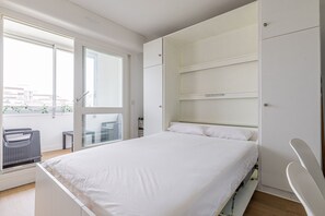 Ein Schlafzimmer mit Bett, Fenster, Balkon und einem eingebauten Kleiderschrank.