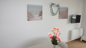Ein Zimmer mit weißer Wand, einem weißen Heizkörper, einem weißen Stuhl und einer rosa Blumenkomposition.