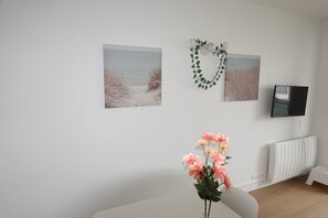 Ein Zimmer mit weißer Wand, einem weißen Heizkörper, einem weißen Stuhl und einer rosa Blumenkomposition.