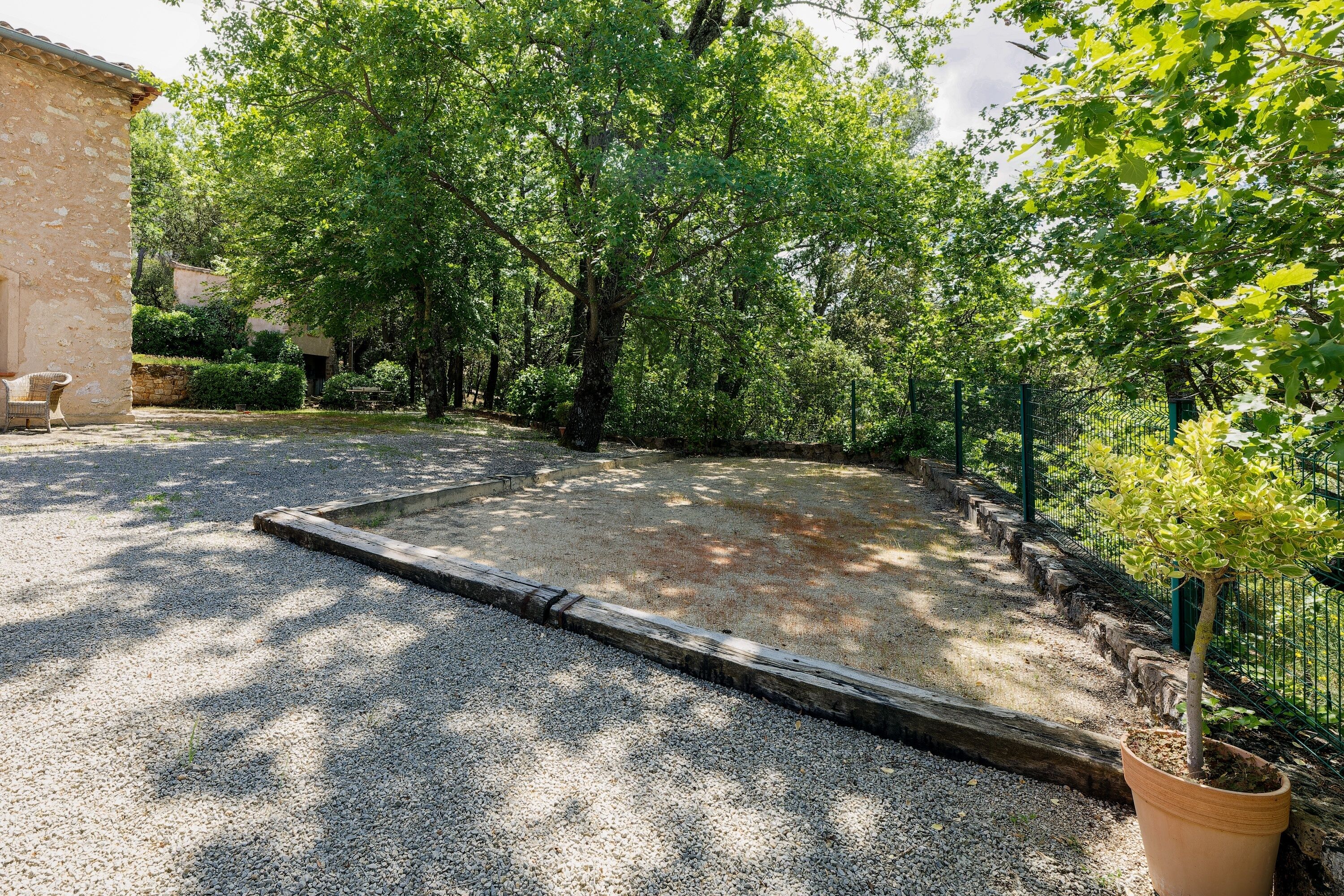 A gravel courtyard with a wooden deck, surrounded by trees and a stone building.