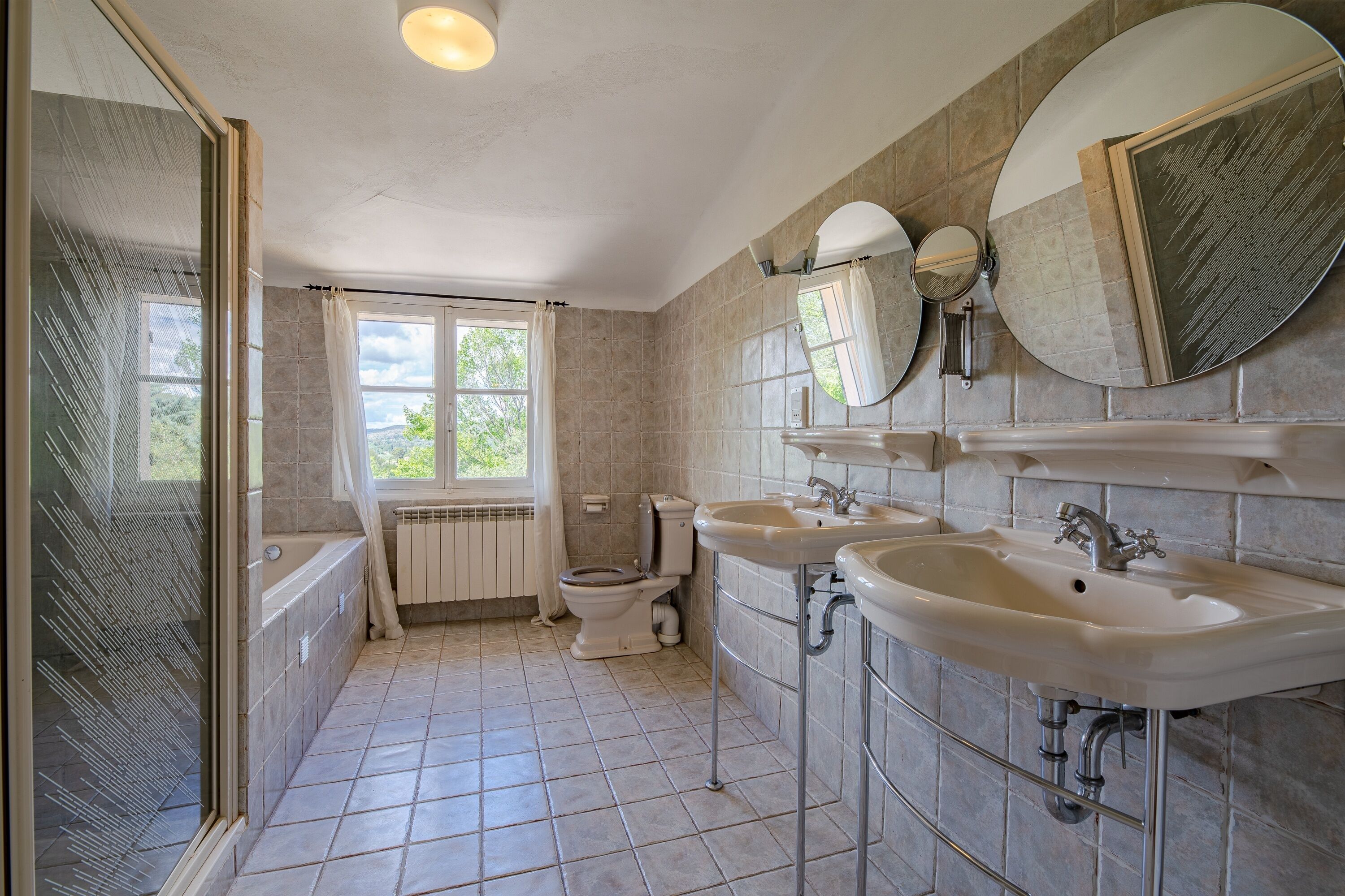 A bathroom with a shower, two sinks, a toilet, and a window.