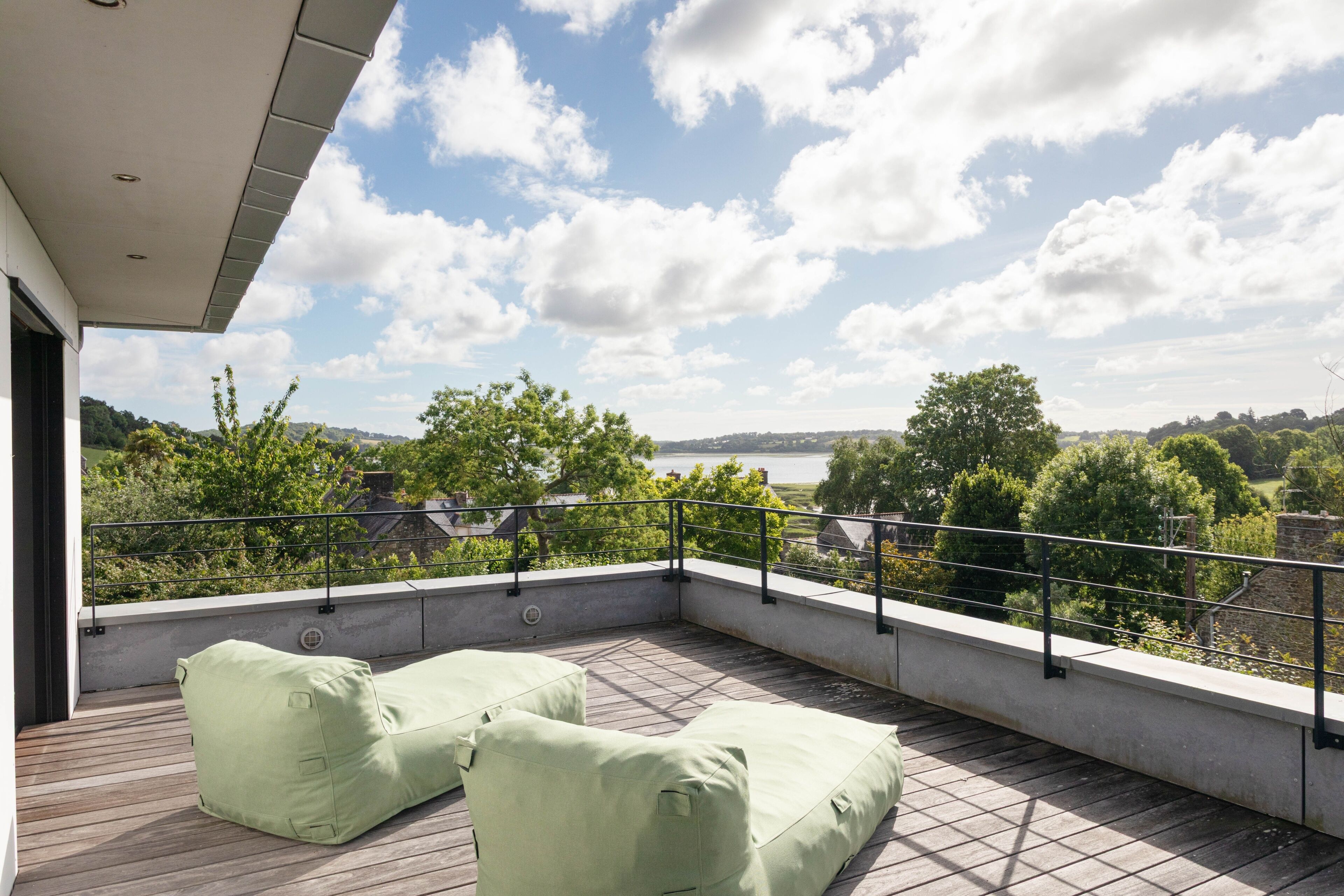 Un balcon extérieur donnant sur un lac, entouré de verdure et agrémenté de sièges confortables aux coussins verts.