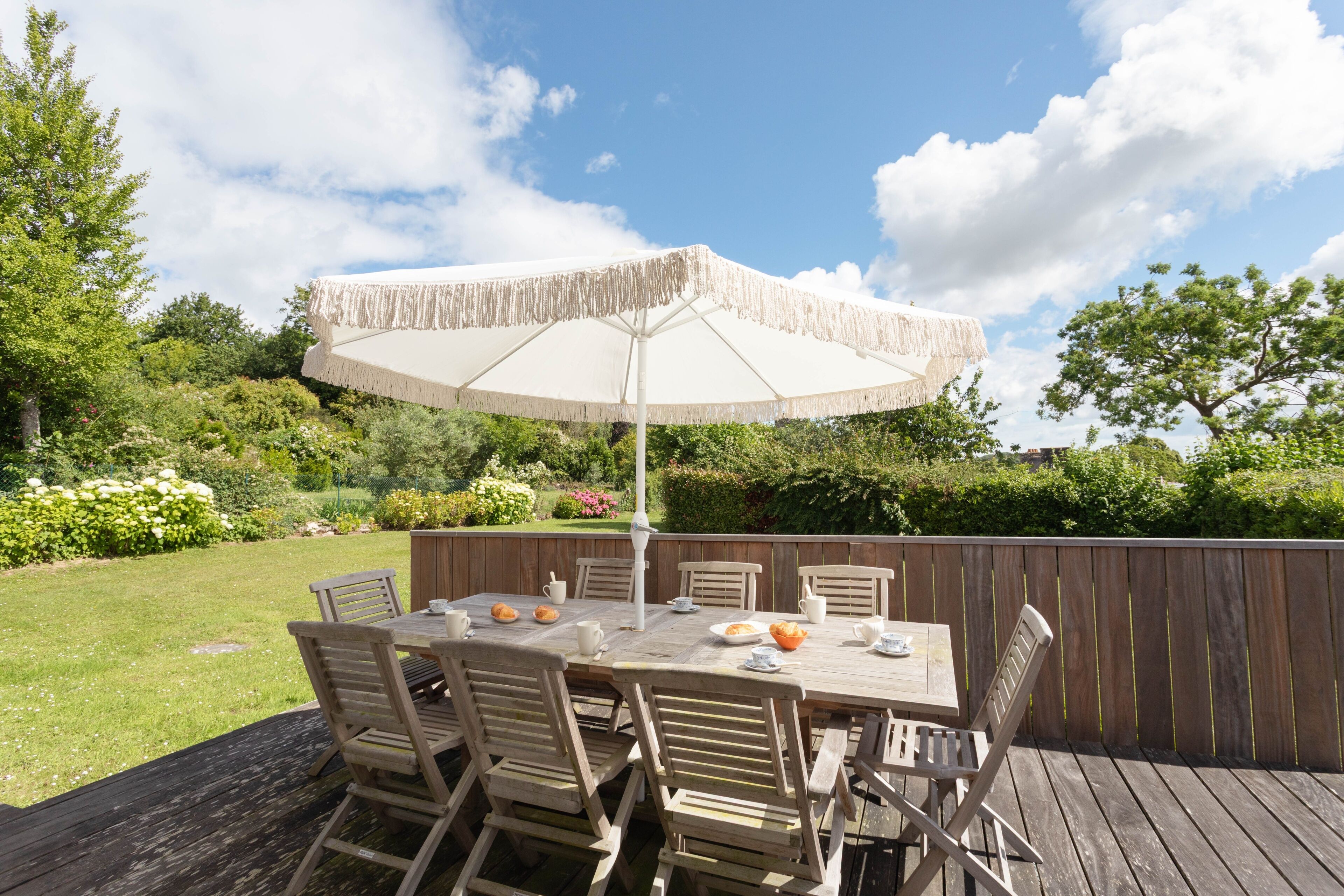 Une terrasse extérieure en bois, avec une table et des chaises, un parasol et une clôture en bois.
