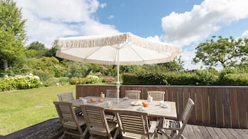 Une terrasse extérieure en bois, avec une table et des chaises, un parasol et une clôture en bois.