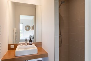 Une salle de bain avec un lavabo blanc, un plan de toilette en bois et une douche aux carreaux bruns.