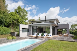 Une maison moderne dotée d’une piscine, d’un espace salon extérieur et d’une grande porte vitrée.