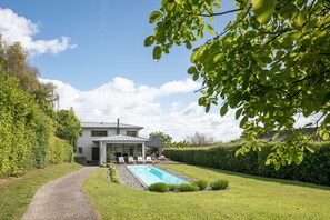 Una casa moderna con piscina, entrada pavimentada y césped cuidado.