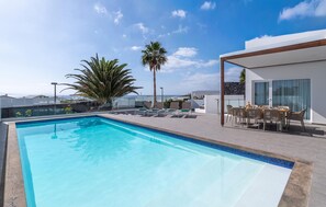 A rooftop pool with clear blue water, surrounded by lounge chairs and a dining area with outdoor seating. - Stunning home in Lanzarote with private swimming pool, can be inside or outside (Lanzarote)