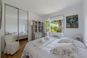 A bedroom with a large mirror, a bedside table with a lamp, a window with a view of greenery, and a painting on the wall. - La Vigie - Ville d'Hiver (Arcachon)