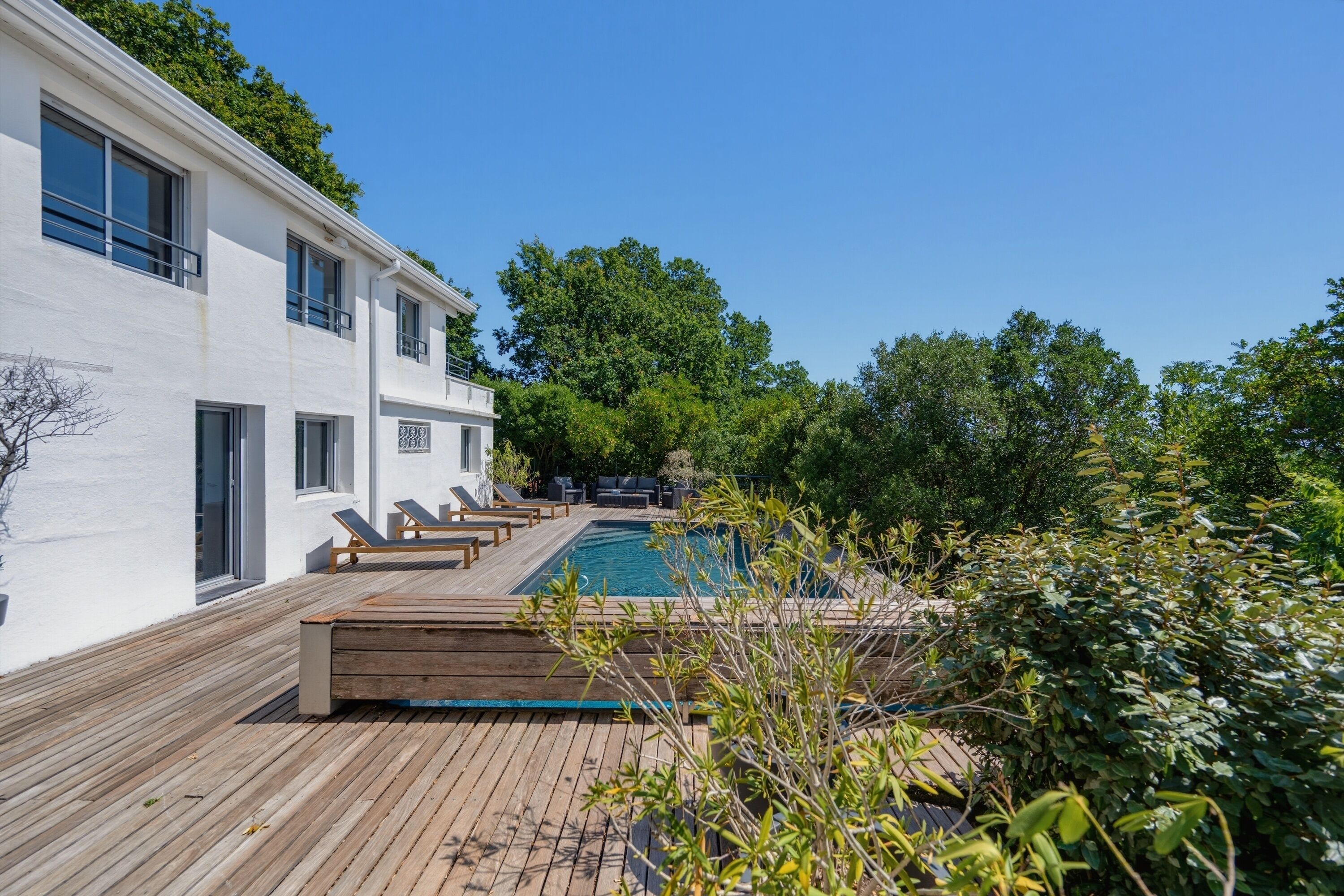Un bâtiment moderne doté d’une piscine, d’une terrasse en bois et d’un espace salon extérieur.