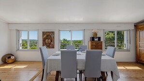 A dining area with a table set for four, large windows, and a view of greenery. - La Vigie - Ville d'Hiver (Arcachon)