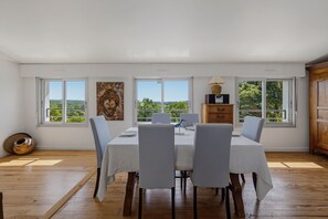 A dining area with a table set for four, large windows, and a view of greenery. - La Vigie - Ville d'Hiver (Arcachon)
