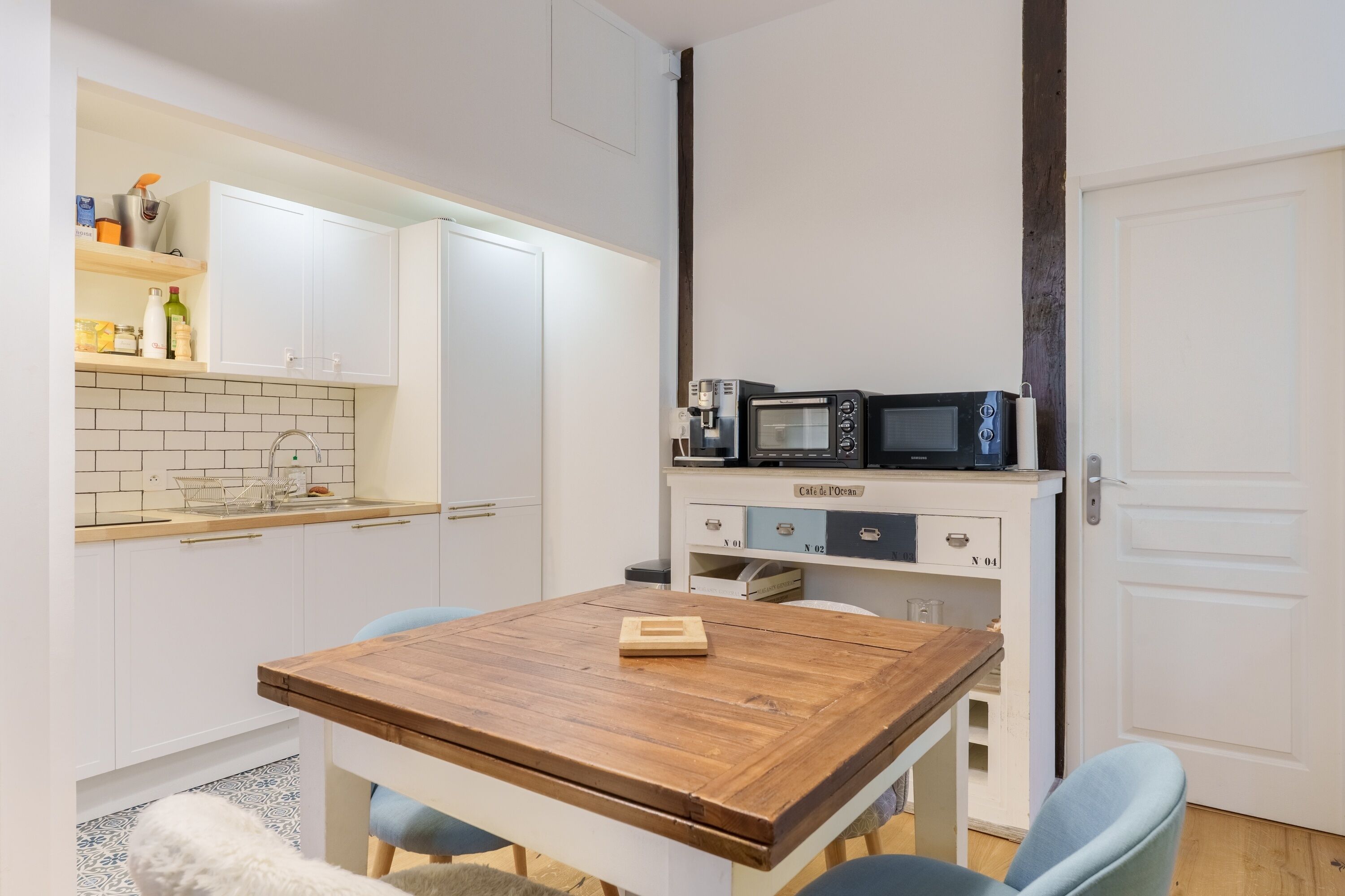 Una cocina compacta con armarios blancos, una mesa de madera y un microondas en la encimera.