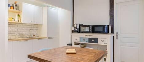 Una cocina compacta con armarios blancos, una mesa de madera y un microondas en la encimera.