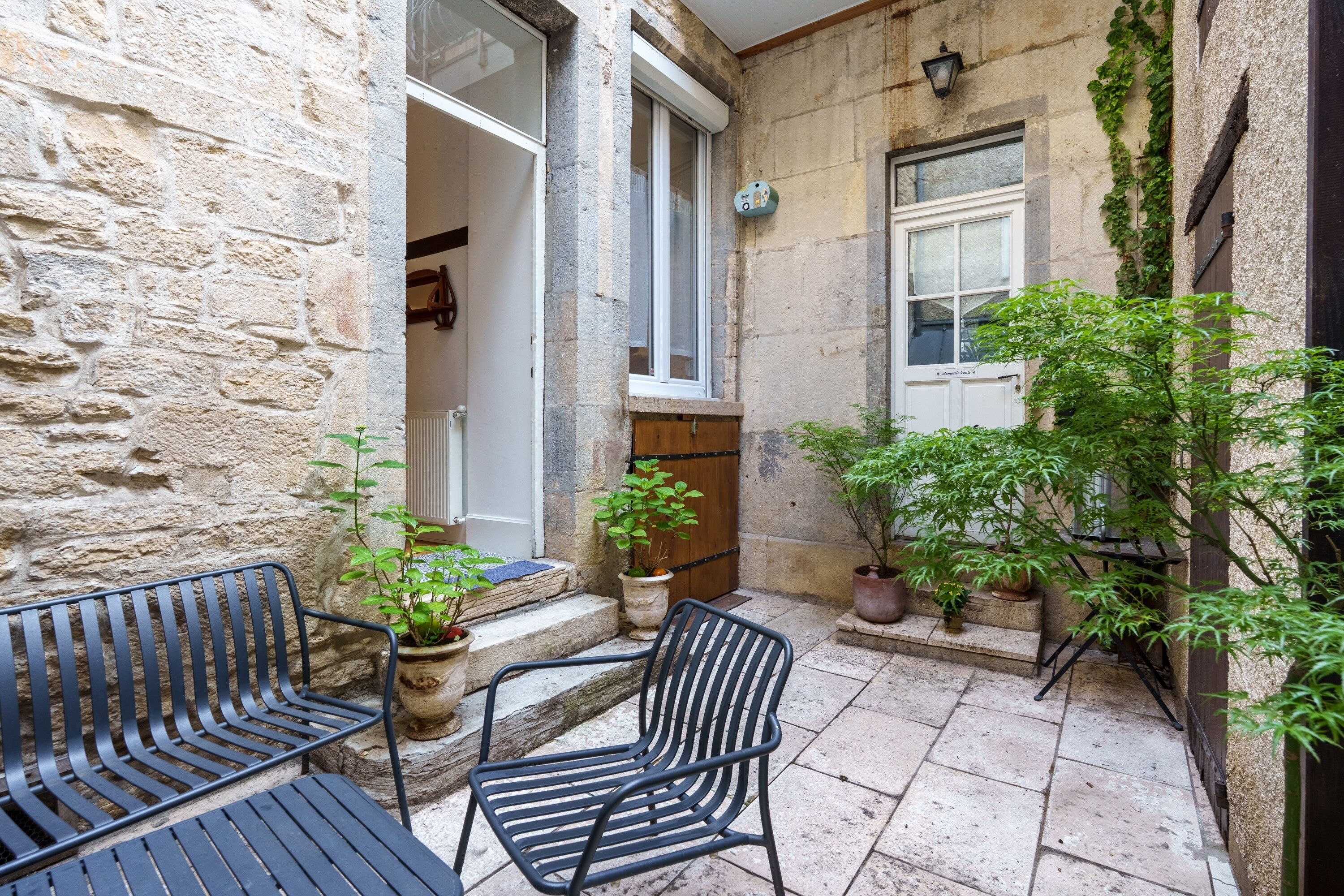 A stone building with a courtyard, featuring a wooden door, potted plants, and outdoor seating.
