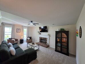 A living room with a sofa, a coffee table, a fireplace, a television, and a dartboard. - Spacious Colonial-style single-family home (Waldorf)