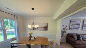 Un comedor con una mesa de madera, cuatro sillas, una araña y un jarrón con flores.