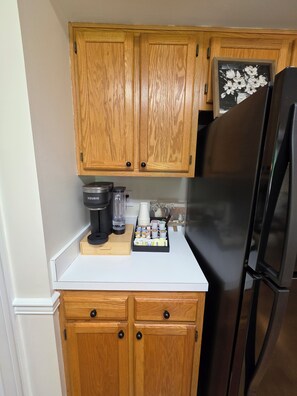 A kitchen with wooden cabinets, a coffee maker, a refrigerator, and a tray of coffee pods. - Spacious Colonial-style single-family home (Waldorf)