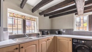 A kitchen with wooden cabinets, a washing machine, and a window with a floral curtain. - Grade II Listed Tudor Charm by Windsor Castle (Windsor)