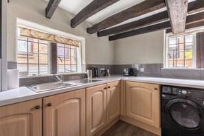 A kitchen with wooden cabinets, a washing machine, a kettle, and a window with a view of a brick building.