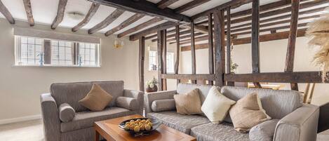 Uma sala de estar com teto de madeira, sofá cinza e mesa de centro de madeira com uma tigela de petiscos.