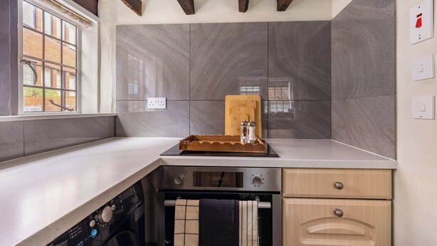A kitchen with a dishwasher, oven, and wooden cutting board on the counter. - Grade II Listed Tudor Charm by Windsor Castle (Windsor)