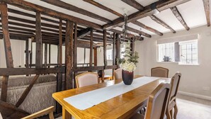 A dining area with a wooden table, chairs, a vase with flowers, and exposed wooden beams. - Grade II Listed Tudor Charm by Windsor Castle (Windsor)