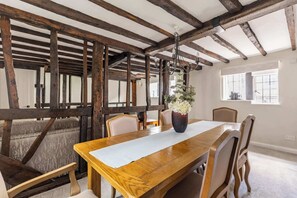 A dining area with a wooden table, chairs, a vase with flowers, and exposed wooden beams. - Grade II Listed Tudor Charm by Windsor Castle (Windsor)