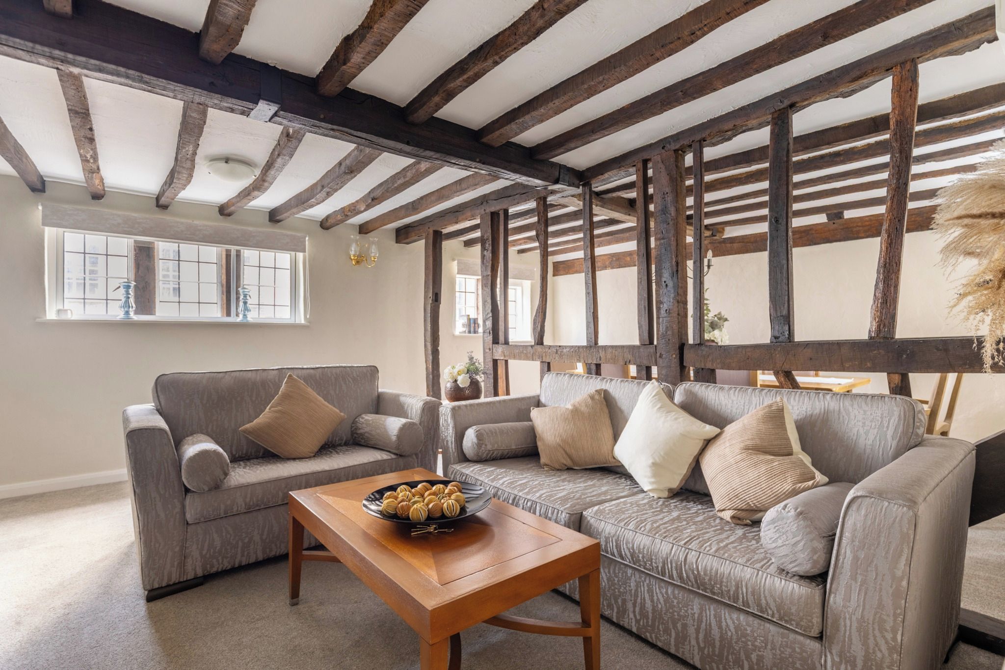 Un salon avec un plafond en bois, un ensemble de canapés gris et une table basse en bois sur laquelle se trouve un bol de collations.