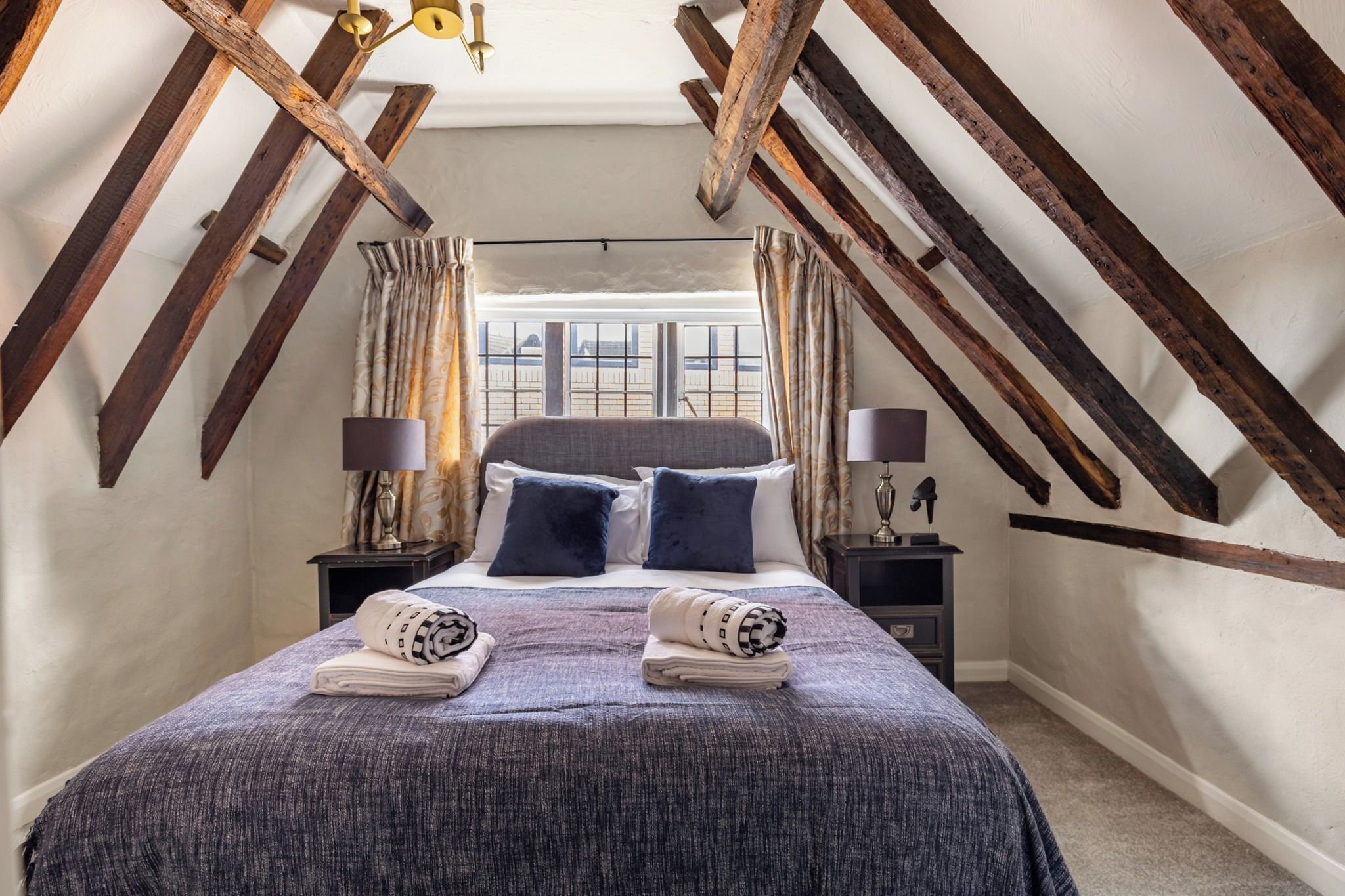 A bedroom with a sloped ceiling, a bed with pillows, two nightstands, and a window with curtains.