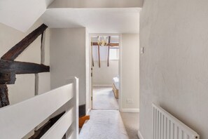 A narrow hallway with a staircase on the left, leading to a bedroom with a bed and a chandelier.