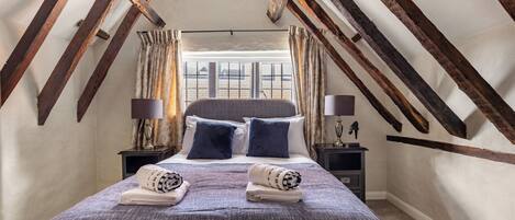 A bedroom with a sloped ceiling, a bed with pillows, two nightstands, and a window with curtains.