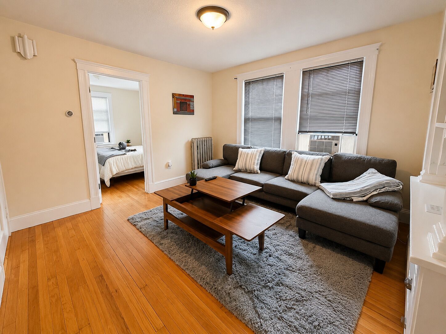 A living room with a sofa, a coffee table, a radiator, and a door leading to a bedroom.