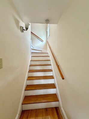 Eine Treppe mit Holzboden und weißen Wänden, ein Geländer auf der rechten Seite und eine Lampe auf der linken.